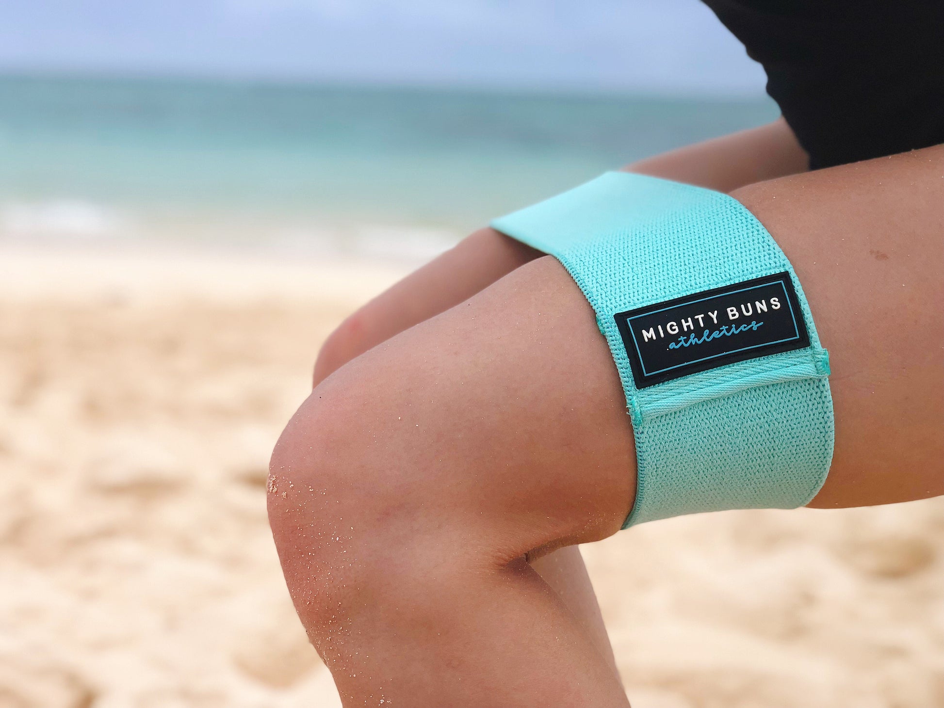 girl squatting at the beach with mint blue heavy-duty resistance band, Mighty Buns
